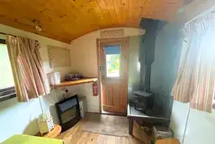 Green shepherd's hut with two single bench beds and a wood burner