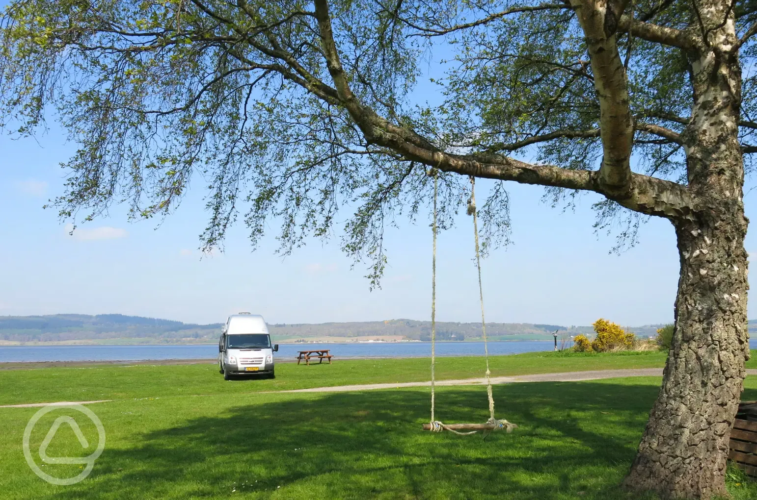 Non electric grass pitches by the waterfront with picnic benches around site