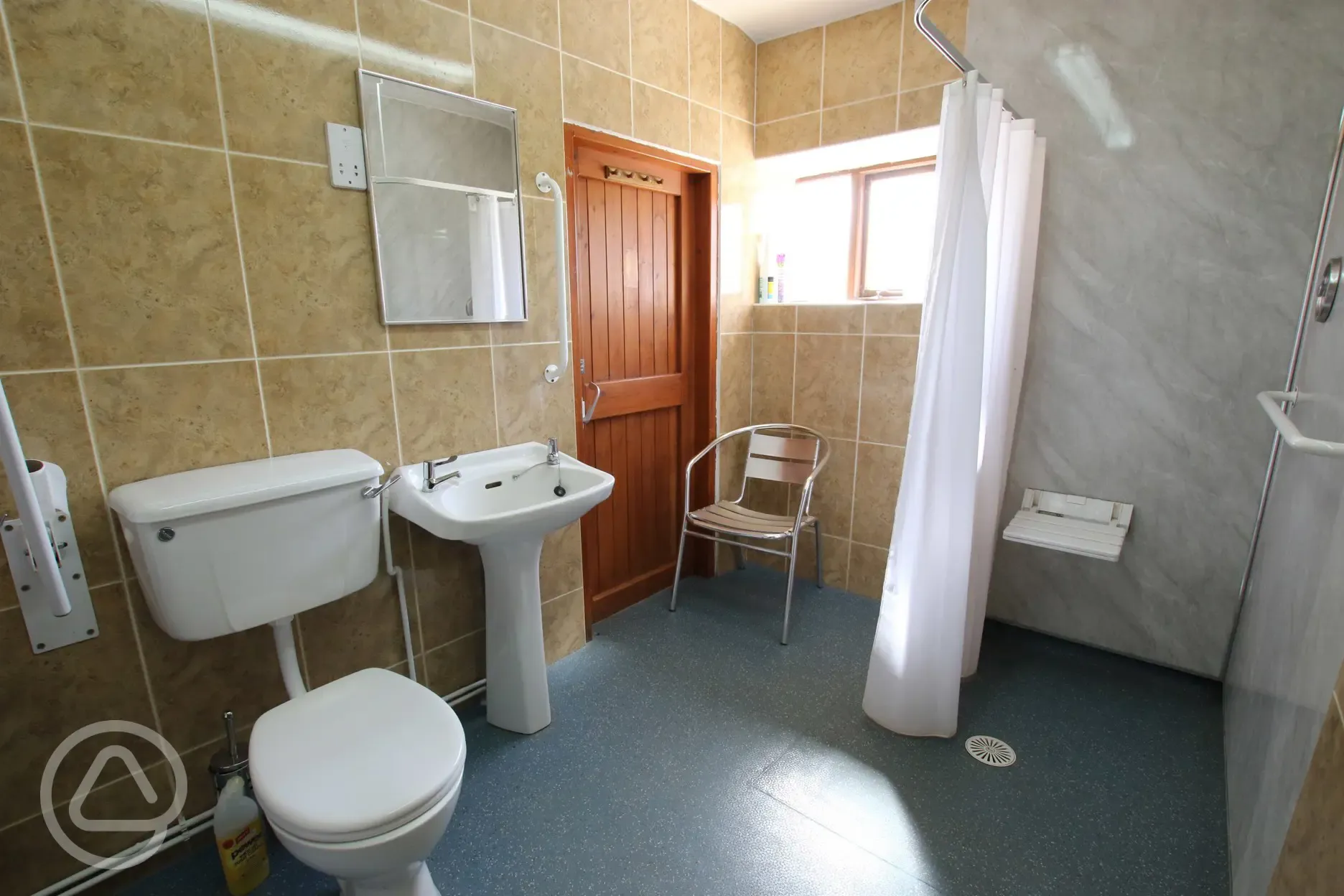 Accessible bathroom with a shower, toilet, grab rails and a chair