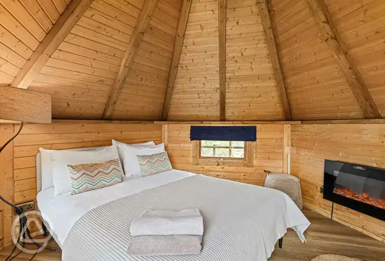 Chestnut glamping cabin interior with double bed and fireplace