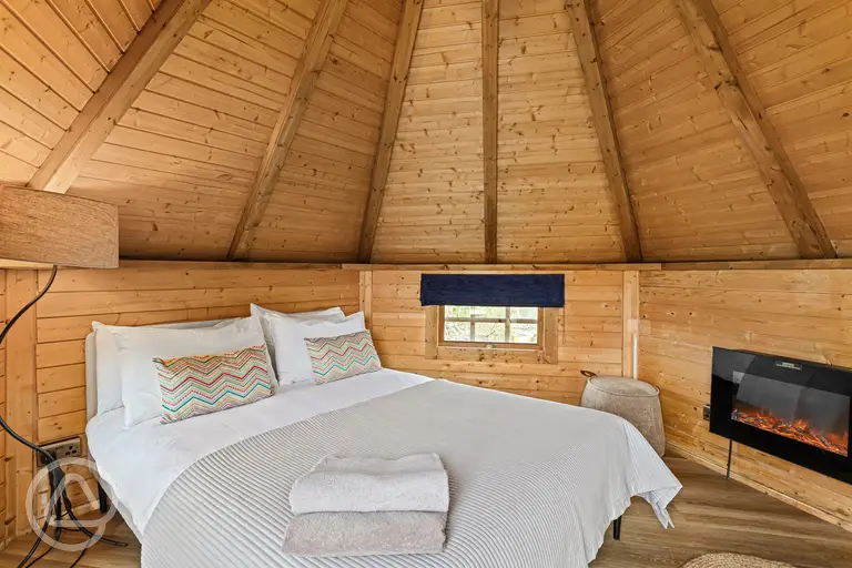 Chestnut glamping cabin interior with double bed and fireplace