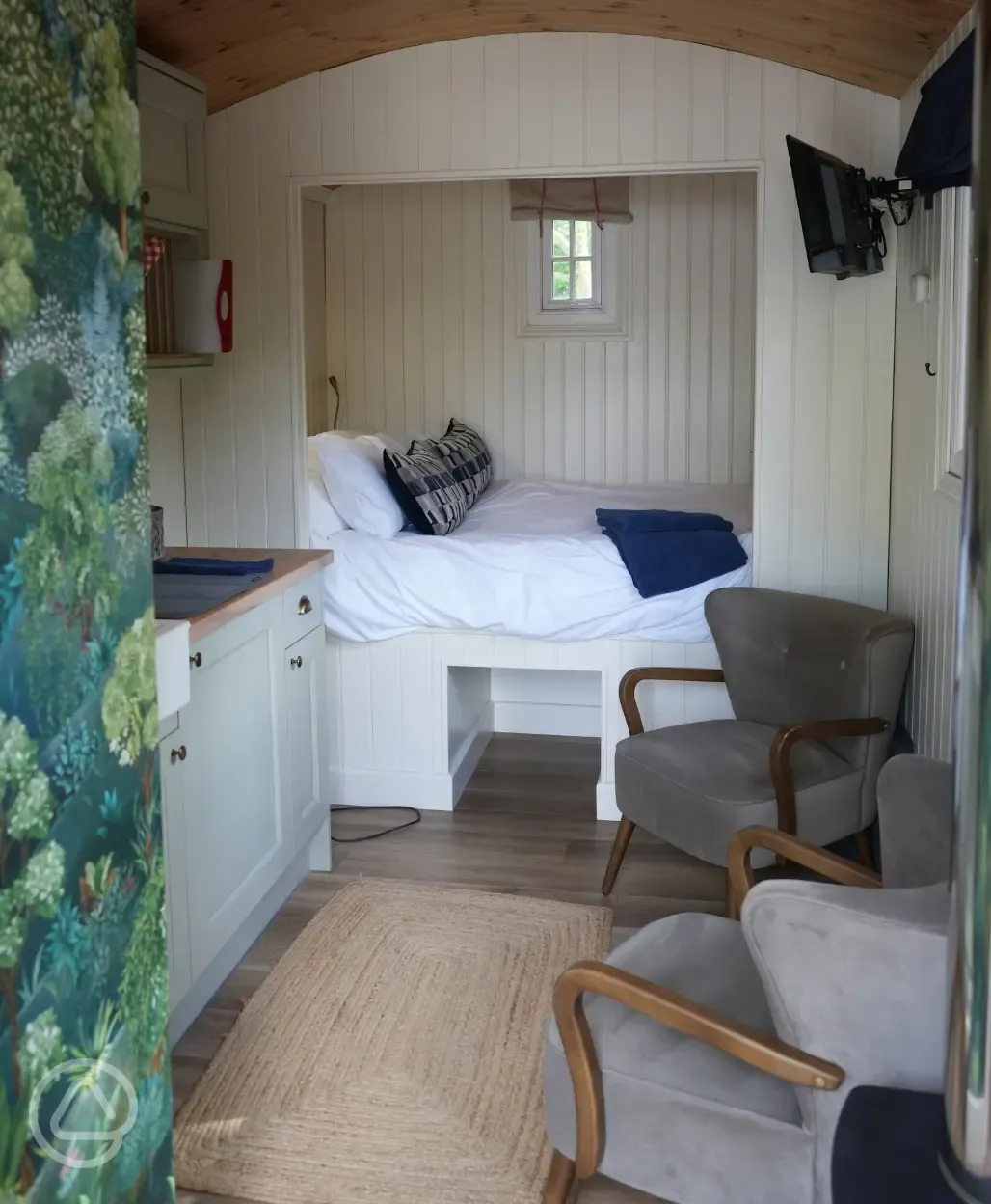 Honey shepherd's hut interior with double bed, seating and kitchenette