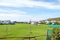 Overview of the camping field with grass pitches and views towards the coast