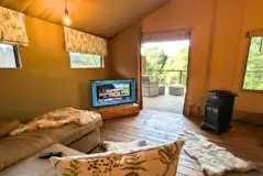 Luxury adult only safari tent interior with an L-shaped sofa, wood burner and TV