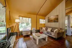 Safari tent living area with a sofa, TV, wood-burner and furnishings