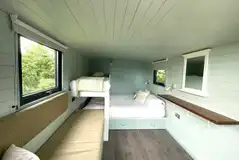 Tawny shepherd's hut with a king sized bed, single bunk, and a convertible