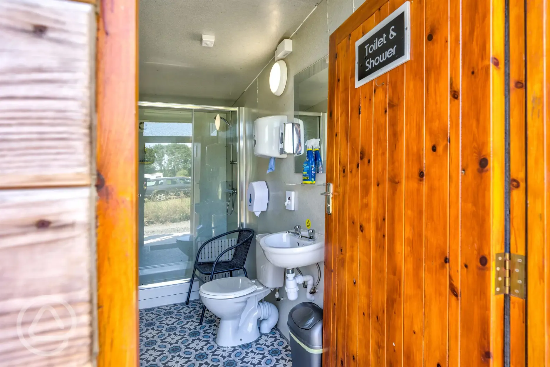 Toilet and shower block with a mirror, a chair, and handwashing sink 