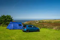 Large tent on grass pitch with space for a parked car