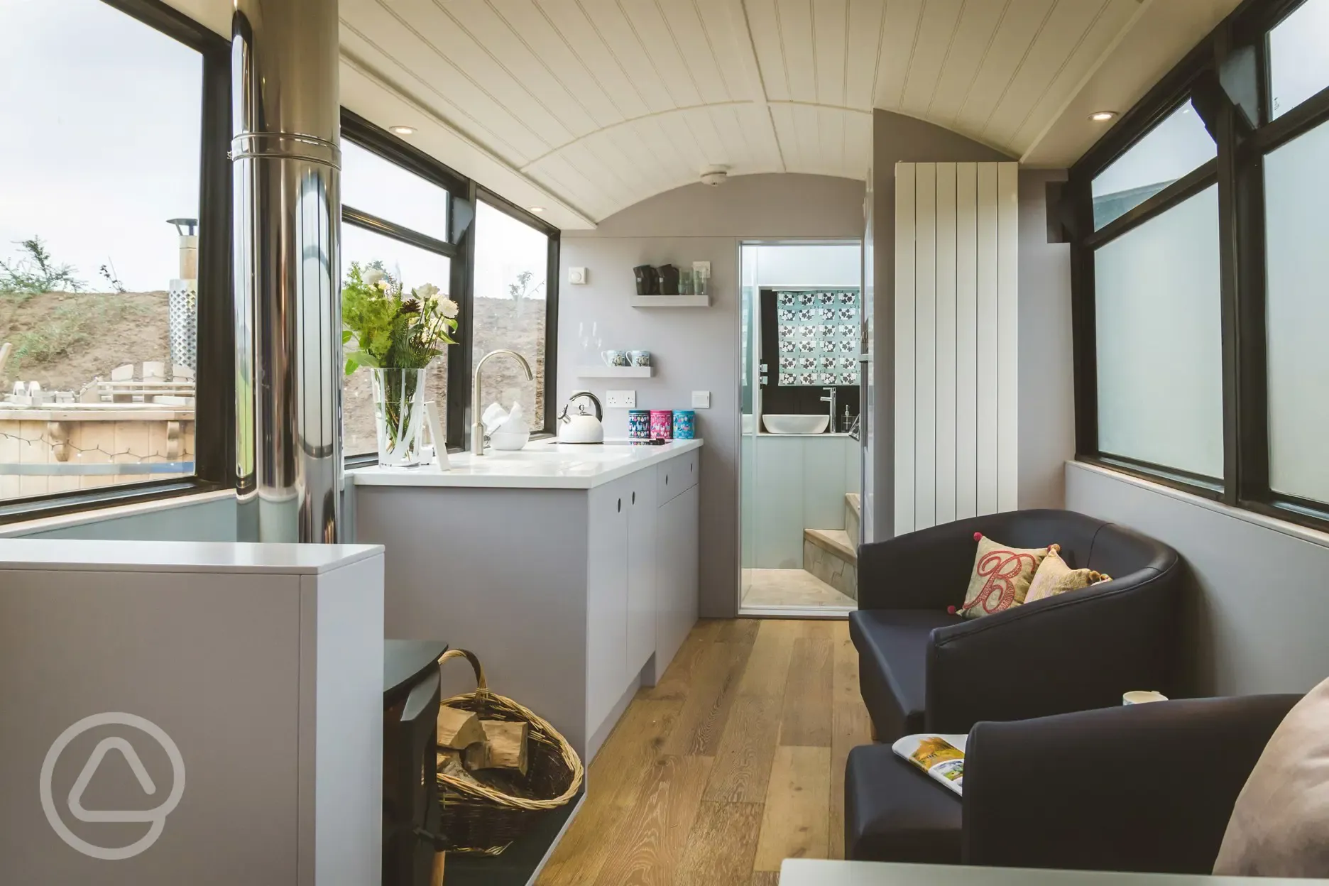 Luxury glamping bus (two person) living area with a log stove, sofa, and kitchen