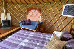 Thistle yurt interior with a single sofa/futon bed and wood burning fire place