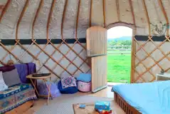 Yurt interior with a double bed, roll mats, log burner and logs