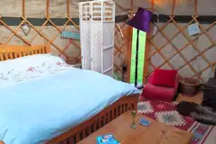 Yurt interior with a double bed, roll mats, log burner and logs