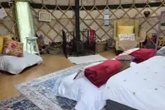 Yurt interior with a double bed, roll mats, log burner and logs