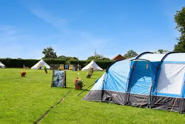 Large tent on a grass pitch with bell tents in the distance