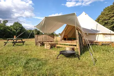 Raised bell tents with a fire pit and fencing at Sunset Tree Camping