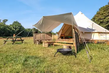 Raised bell tents with a fire pit and fencing at Sunset Tree Camping