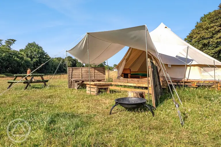 Raised bell tents with a fire pit and fencing at Sunset Tree Camping