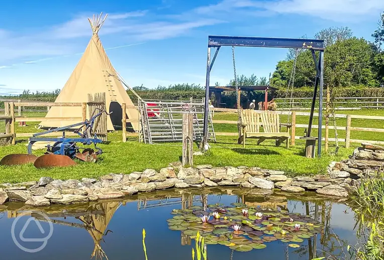 Tipi tent exterior with pond and swing