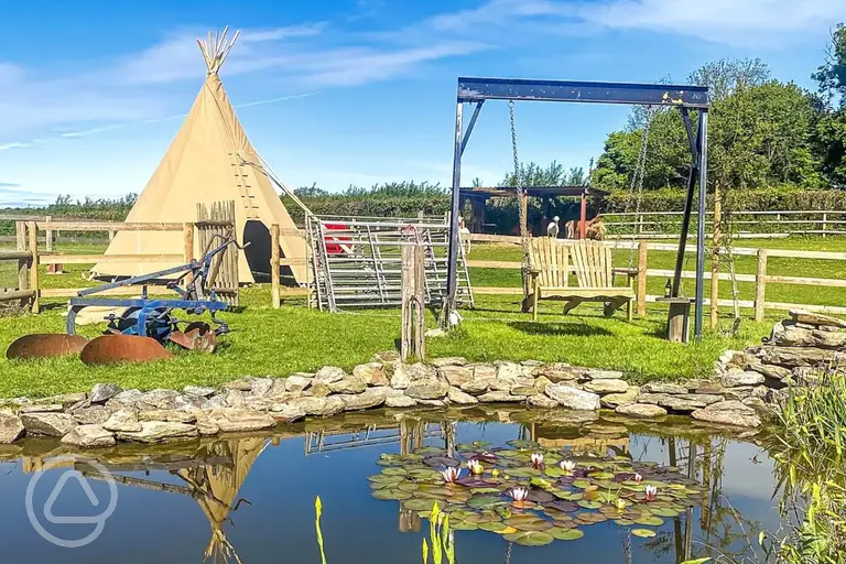 Tipi tent exterior with pond and swing