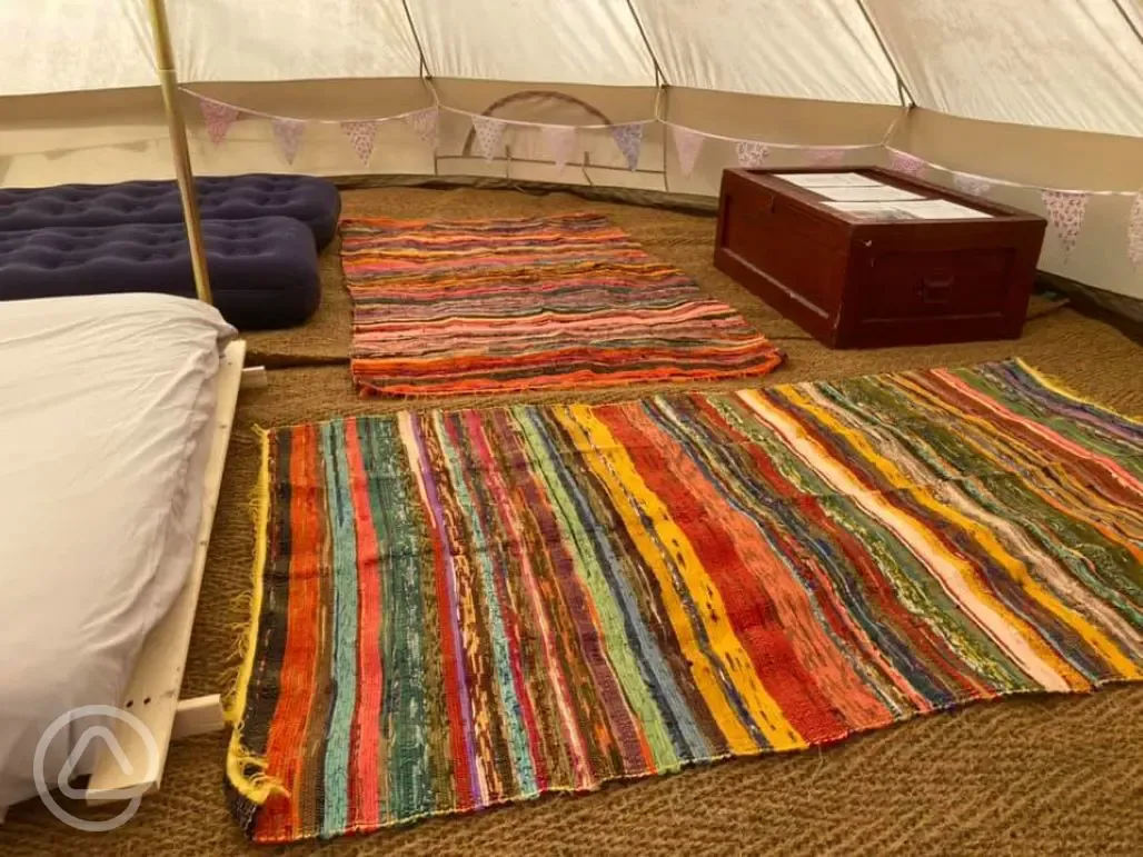 Bell tent interior furnished with airbeds, futons, and rugs