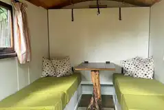 Green shepherd's hut with two single bench beds and a wood burner